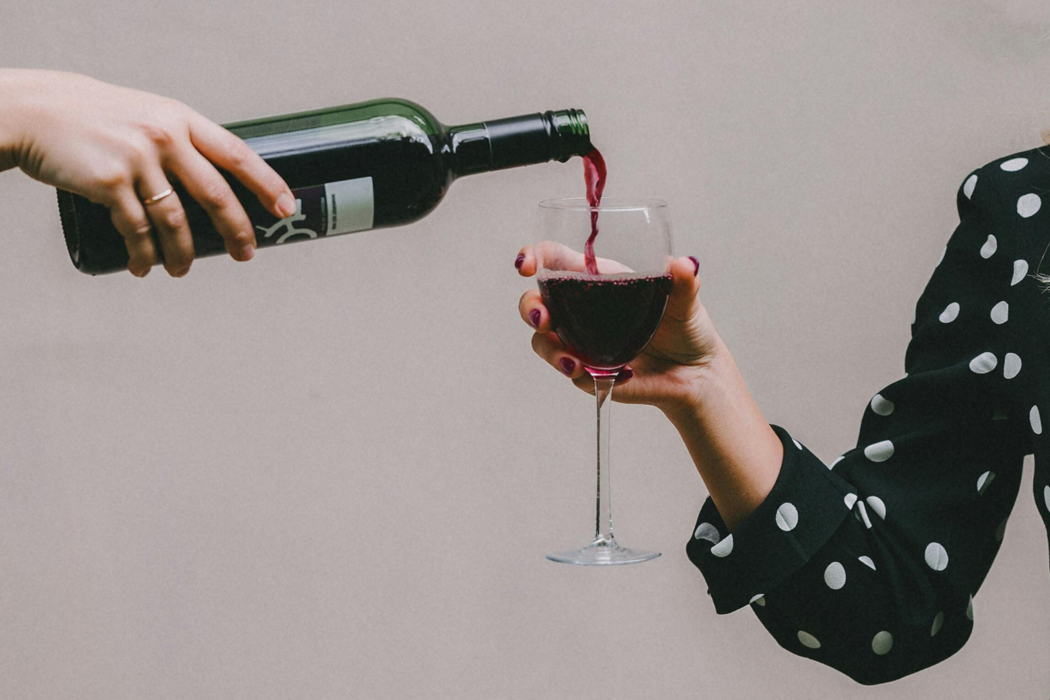 Someone pouring a bottle of red alcohol free wine in a wine glass held by a woman in a black shirt